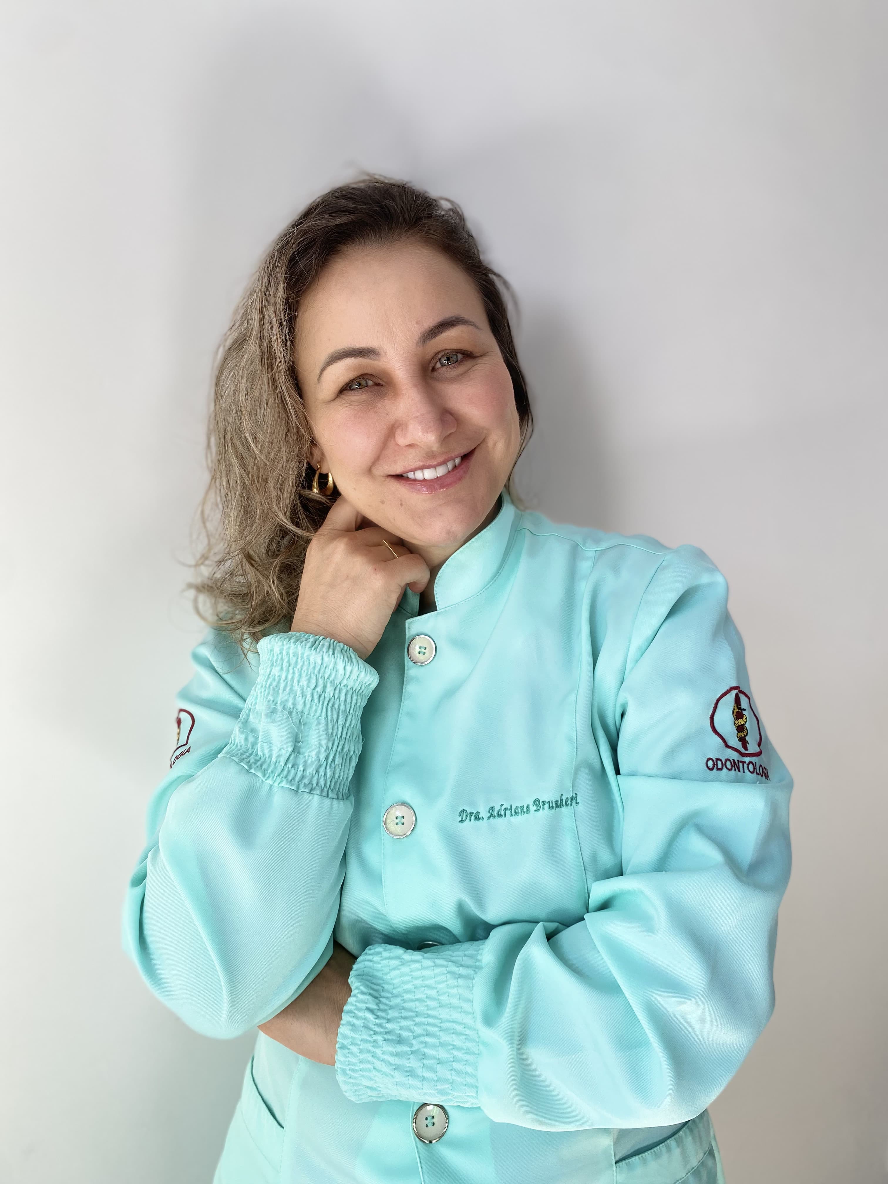 Dra. Adriana Brunheri, cirurgiã-dentista, sorrindo com jaleco verde-água